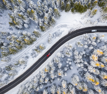 Punainen ja valkoinen auto lumisella metsätiellä kuvattuna ylhäältä.