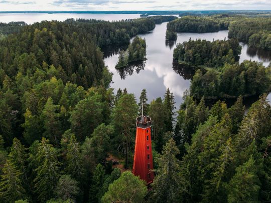 Punainen tähystystorni metsässä järven rannalla.